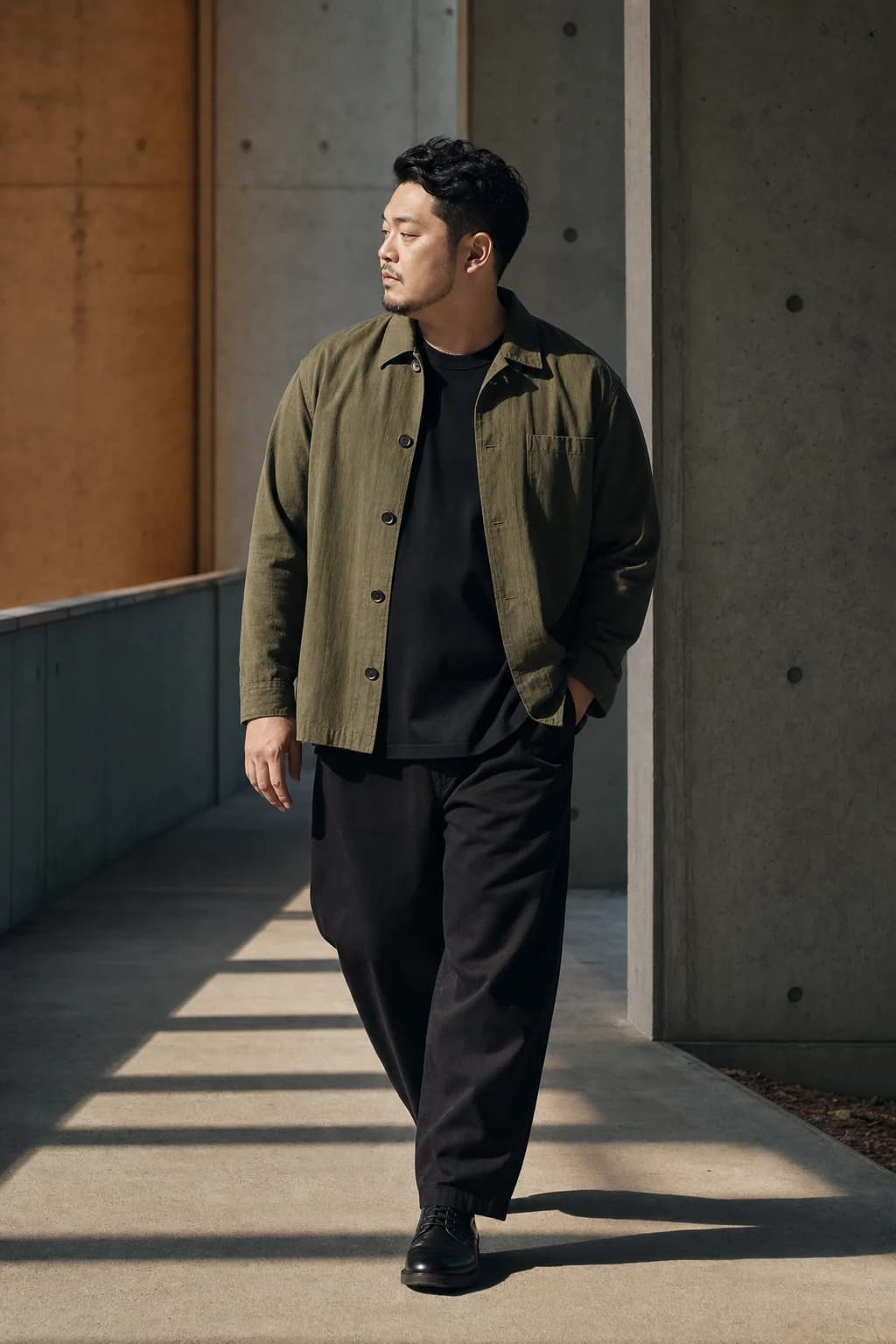 Man in an olive overshirt walking through a concrete corridor